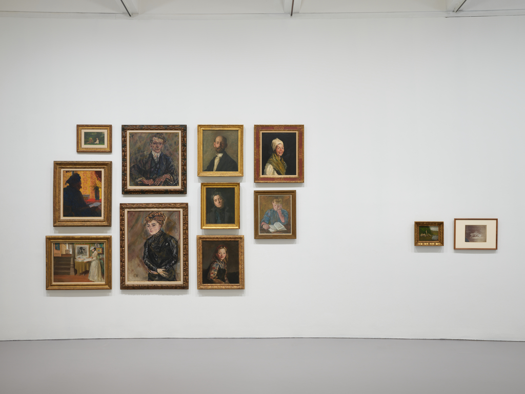 a wall covered in 12 small and medium portraits of white men, women and children.