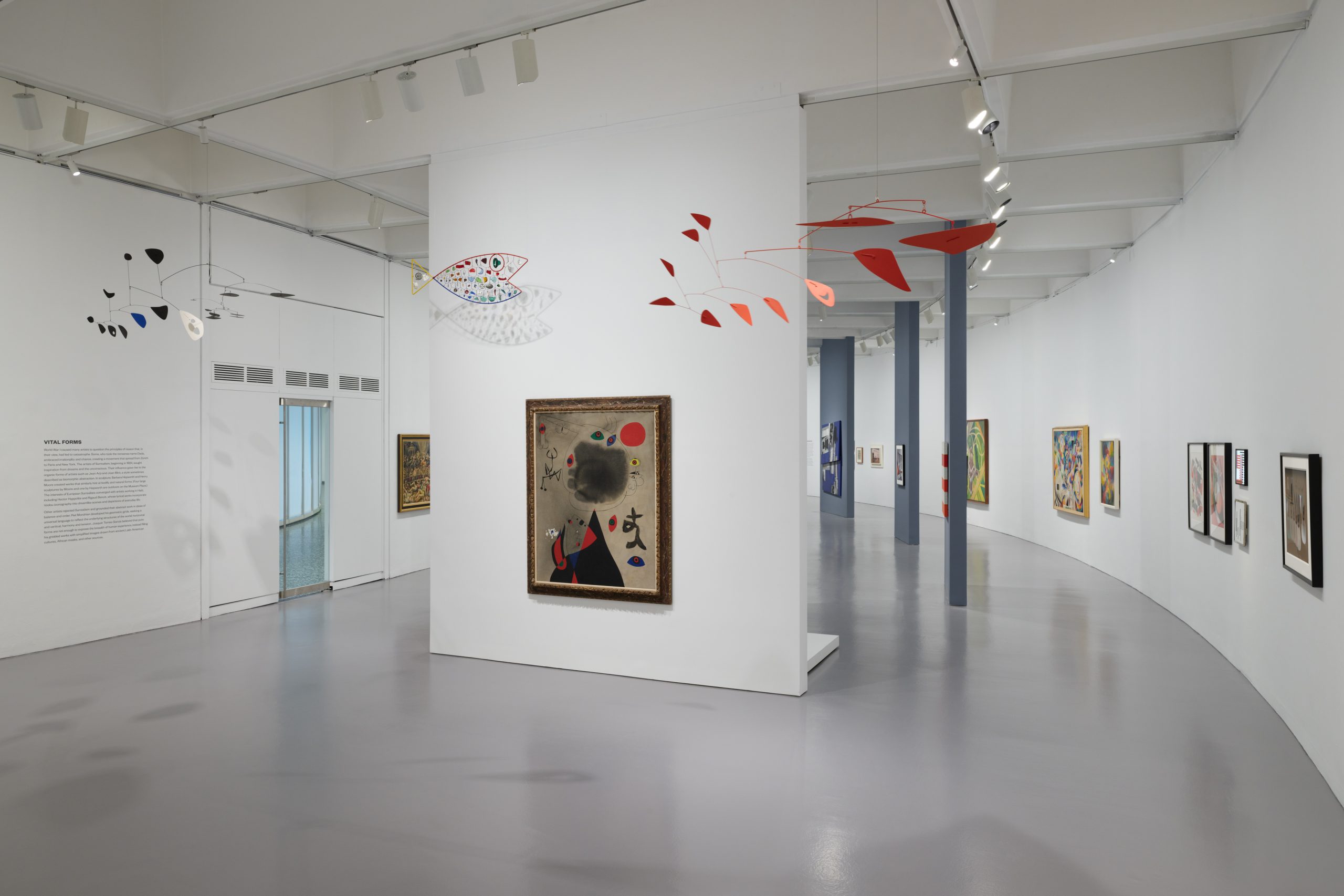 Installation view of Calder Mobiles hanging from the ceiling, surrounded by surrealist artwork from Joan Miro and Max Ernst.