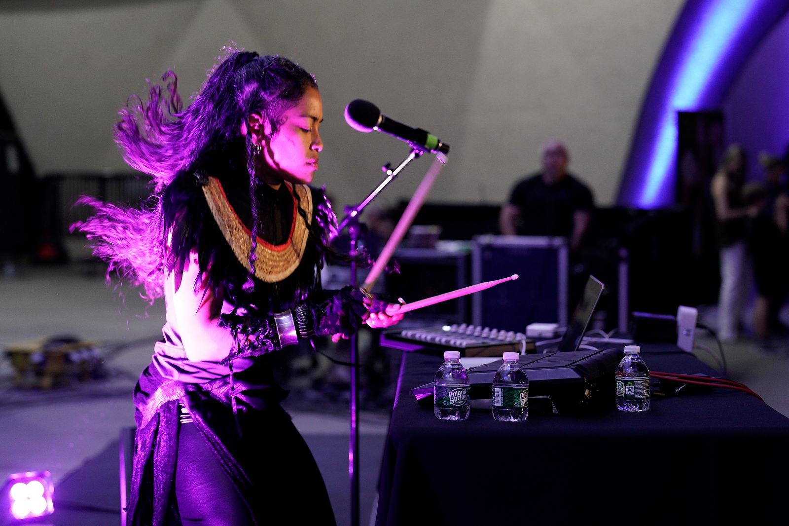 Person drumming on a machine on a table. Dimly lit by purple light.