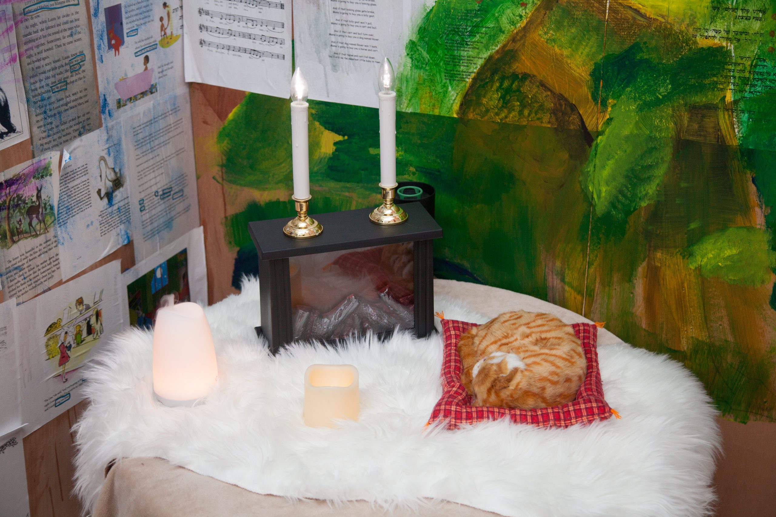 A shrine is placed in the corner of a room. Objects have been placed on a round surface covered by a white fluffy blanket.