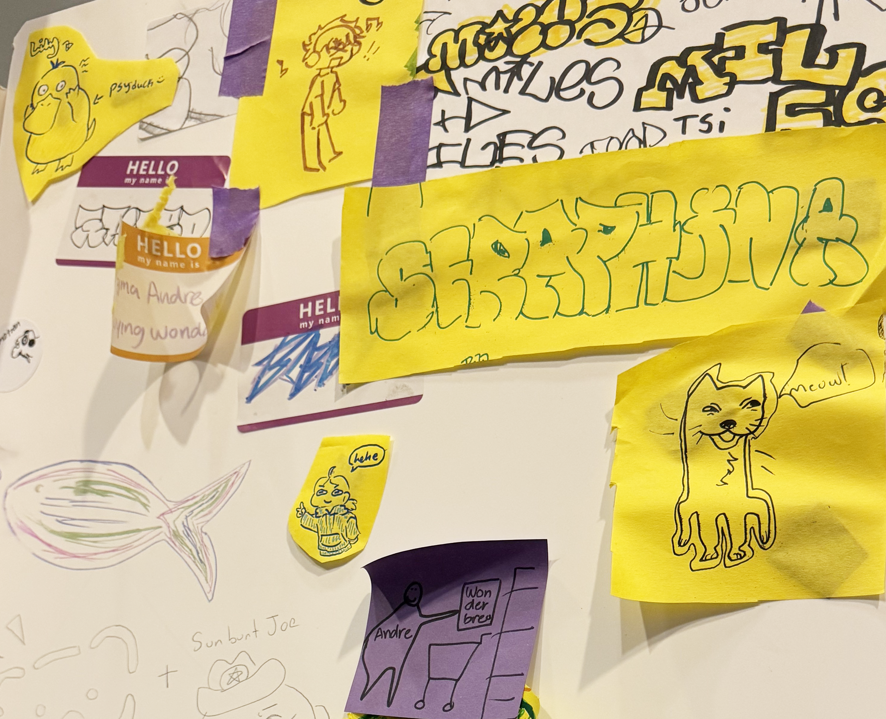 Drawings on yellow construction paper in various sized cutout pieces and on hello stickers have been taped onto a white board with thick purple masking tape.