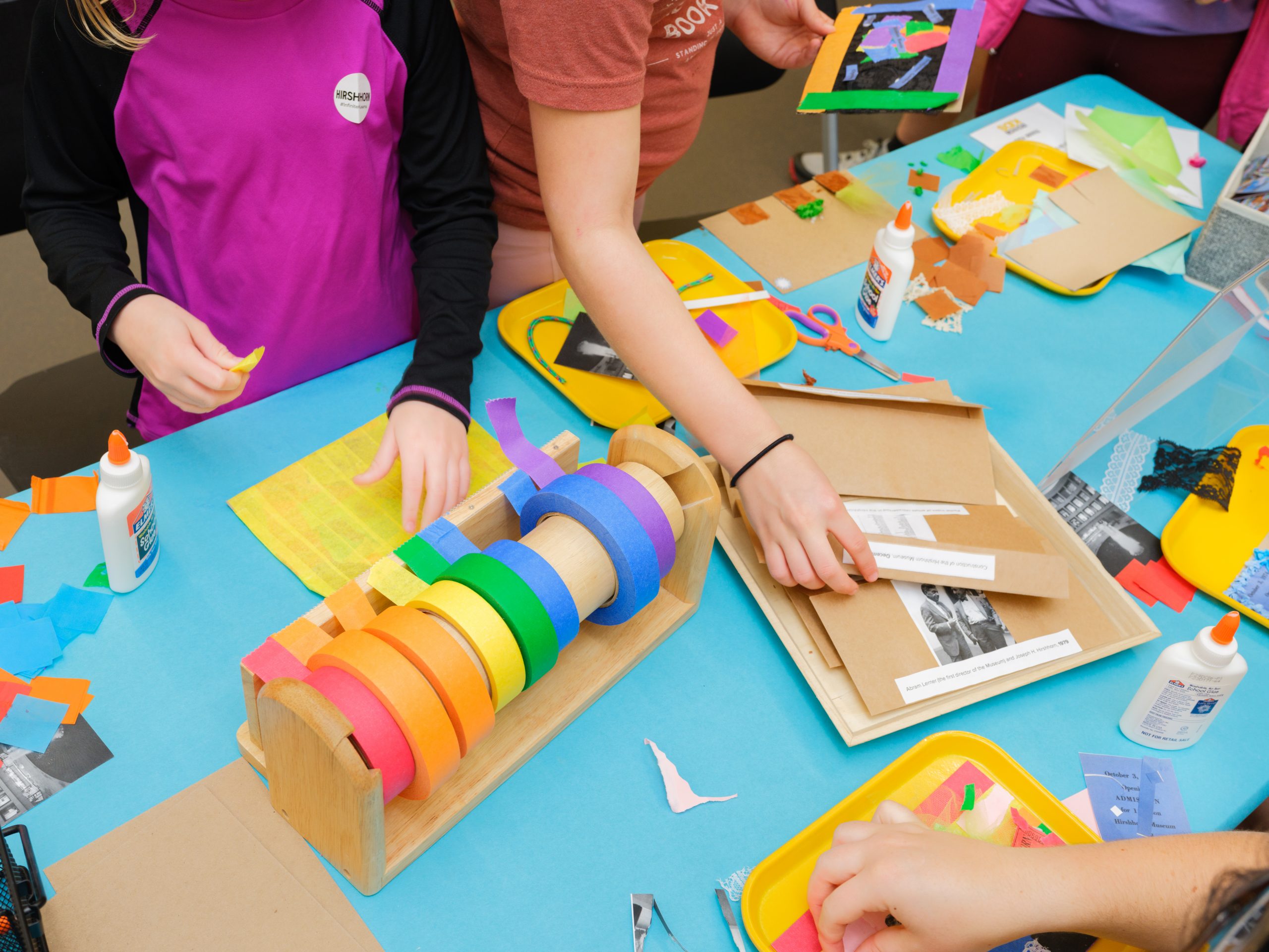 colorful tape, glue, and other art making materials are laid out on a blue table