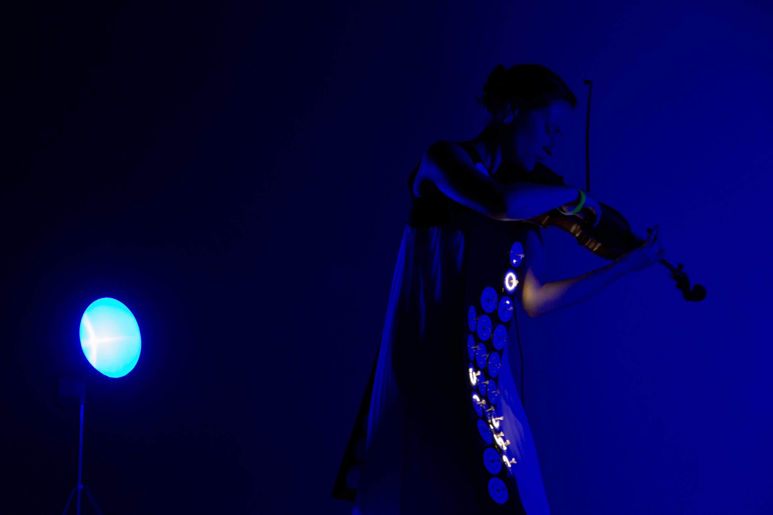 a woman plays a violin in a dark blue lit room