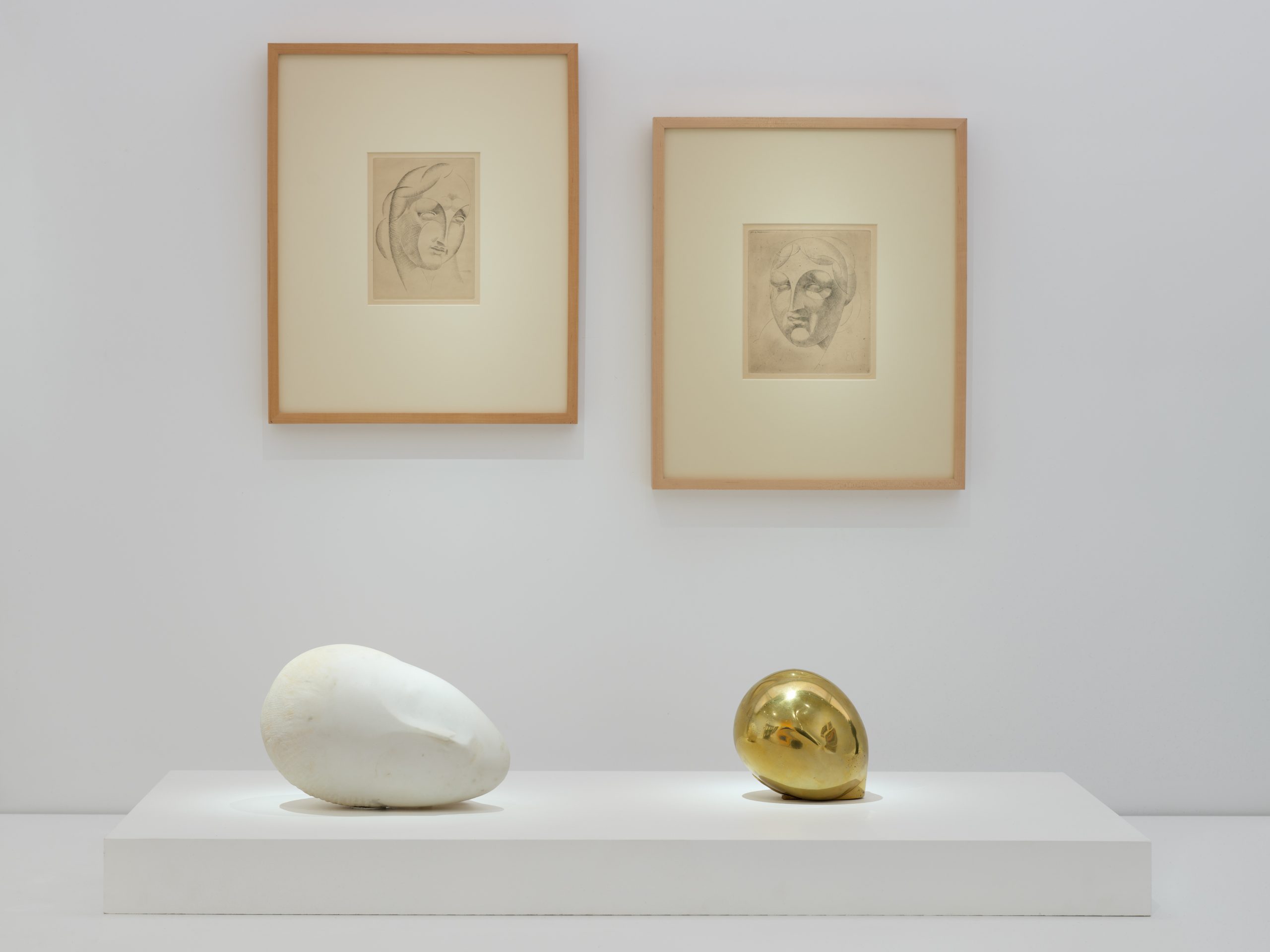 two drawings of heads are placed directly above two sculptures of heads, one marble, the other gold.