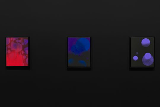 Three colorful paintings displayed on a black wall, showcasing vibrant reds, blues, and purple geometric triangles and circles