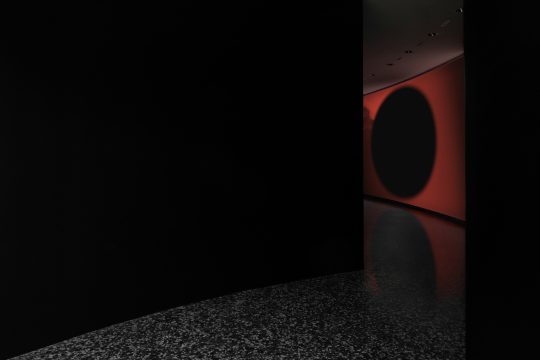 A black room featuring a prominent large black circle in the center of a red screen, creating a striking visual contrast.