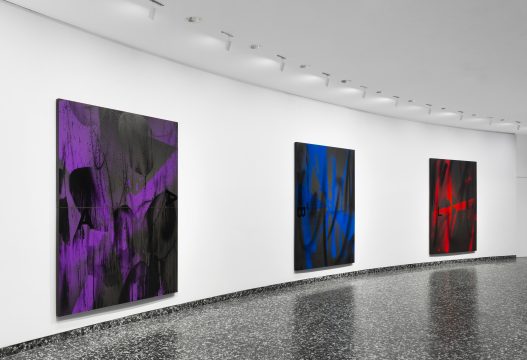 three large vertical canvases are showcased on the wall. They feature black and purple abstract marks, blue and black abstract marks, and black and red abstract