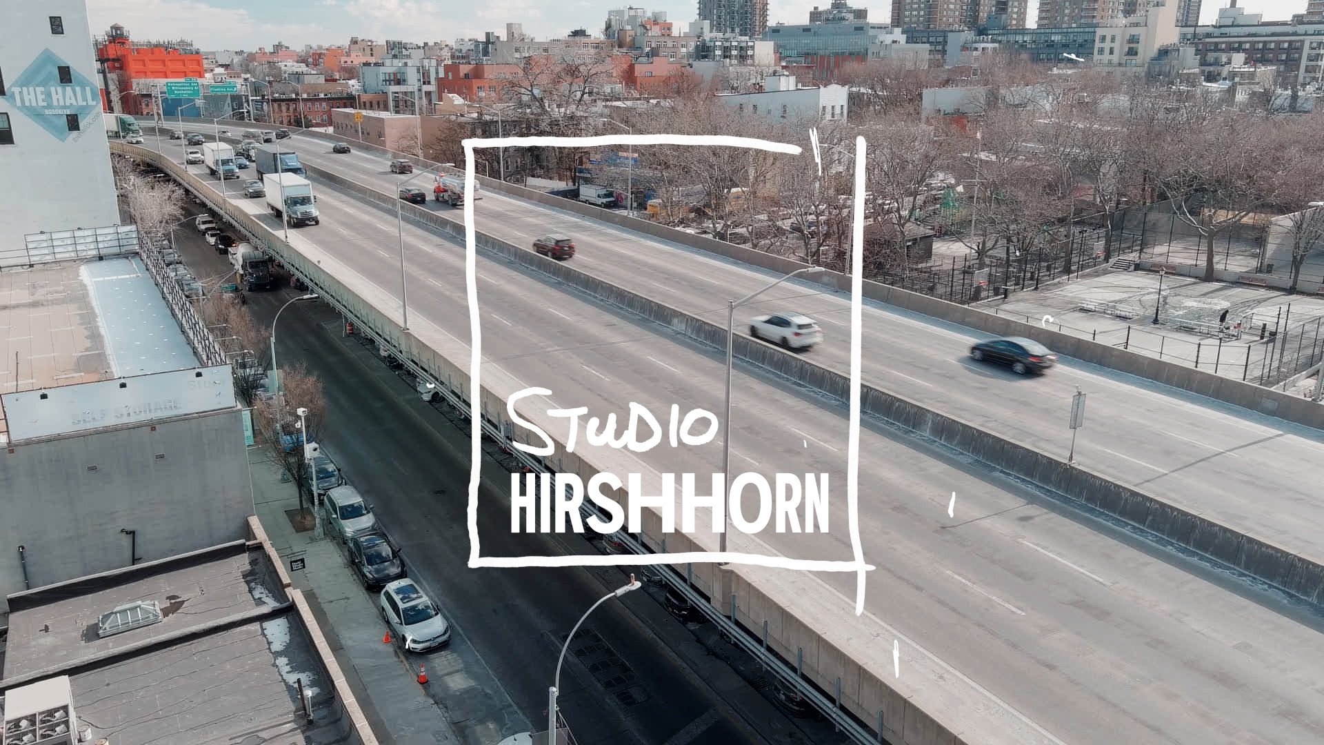 Screen capture of a video shows a city view featuring a highway and a box graphic in the middle that read Studio Hirshhorn